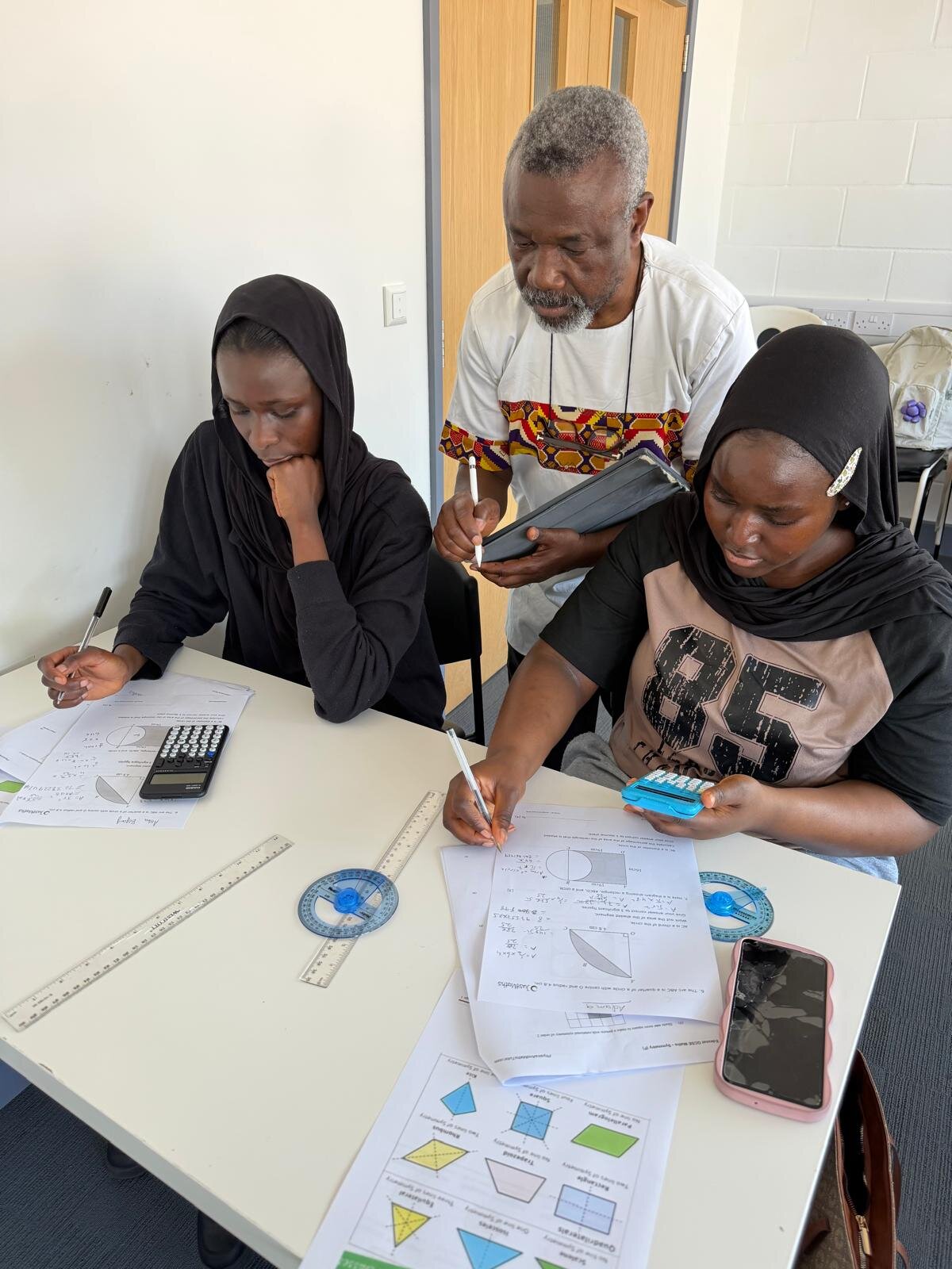 Sylvester Peprah guiding two GCSE students through geometry worksheets in the classroom